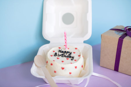 Birthday cake Bento in eco-packaging with a wooden spoon with a candle next to a gift on a purple backgroundの写真素材