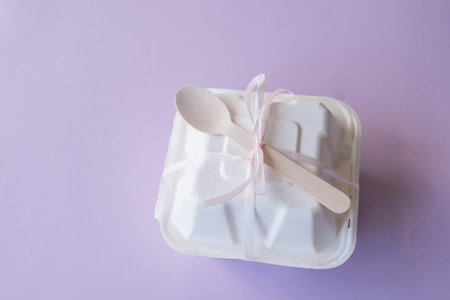 A gift box for a bento cake with a wooden spoon stands closed on a purple backgroundの写真素材