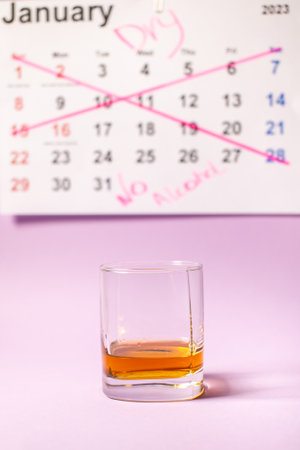 A glass of whiskey stands against the background of a crossed-out calendar for January, challengeの写真素材