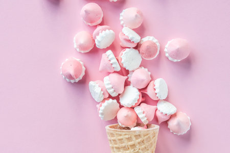 Multicolored pink and white meringues in waffle cookies lie scattered on a pink backgroundの写真素材