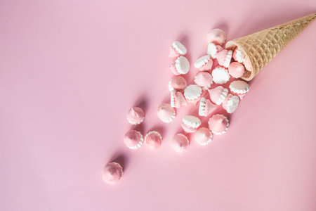 Multicolored pink and white meringues in waffle cookies lie scattered on a pink backgroundの写真素材