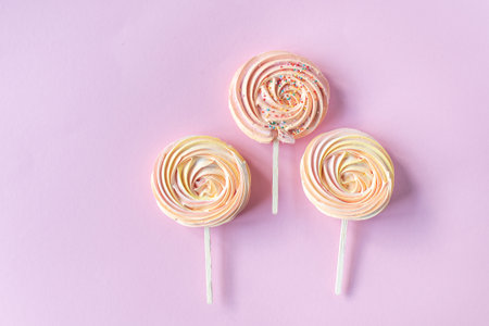 Pink round sweet meringues on a stick with decor lie on a pink backgroundの写真素材