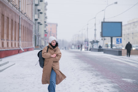 A cute girl in a coat is walking around the city in bad cold weather. Carry a backpackの写真素材