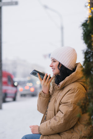 A young girl in a warm hat and coat records a voice message outside in winter and laughsの写真素材