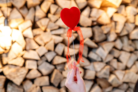 A red heart on a stick is held by a woman's hand. Firewood backgroundの写真素材