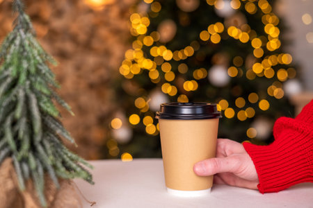 A disposable cup with a lid should be placed hand on the table near the Christmas treeの写真素材