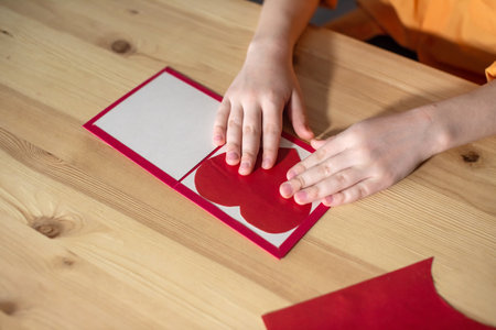 Children's hands make a postcard with a red heart of colored paperの写真素材
