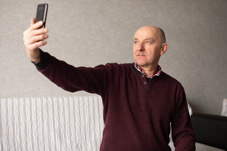 An adult man takes a selfie on his phone in the living roomの写真素材