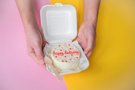 A man 's hands are holding a festive bento cake with birthday and hearts . Wooden spoon in a boxの写真素材