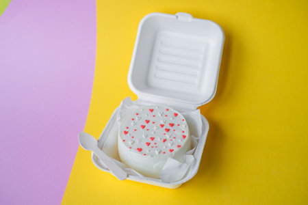 A small bento Valentine's day cake in a box with a wooden spoon. Yellow and pink backgroundの写真素材