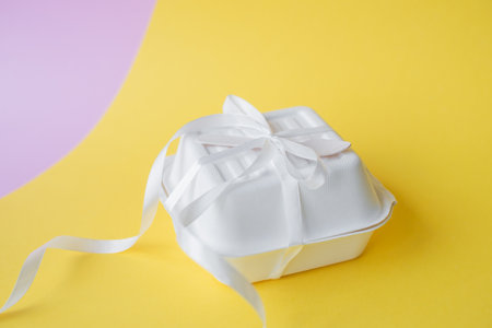 Gift box for a small bento cake with a wooden spoon stand, closed on a yellow backgroundの写真素材