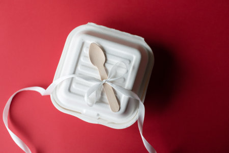 A closed bento cake box with a wooden spoon on a yellow and pink background. White ribbon for giftsの写真素材