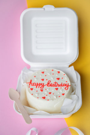 An open box with a birthday bento cake stands on a yellow backgroundの写真素材