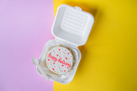 A small bento birthday cake in a box with a wooden spoon. Yellow and pink backgroundの写真素材