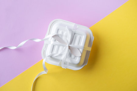 A closed bento cake box with a wooden spoon on a yellow and pink background. Ribbon for giftsの写真素材