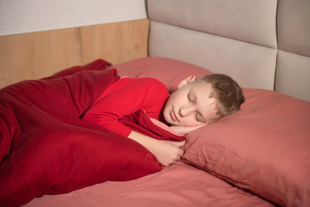 Cute boy sleeping in a bed with red bed linen in pajamasの写真素材