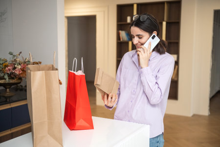 Cute girl is holding a kraft bag of takeaway food in the kitchen and talking on the phone