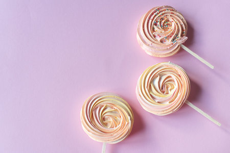 Pink round sweet meringues on a stick with decor lie on a pink backgroundの写真素材
