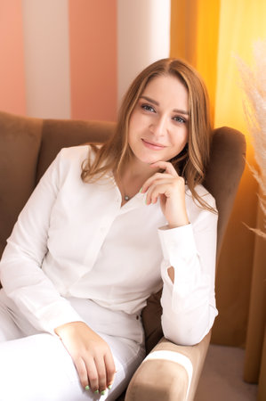 Portrait of a cute girl sitting in a chair, hand under her face. White clothes