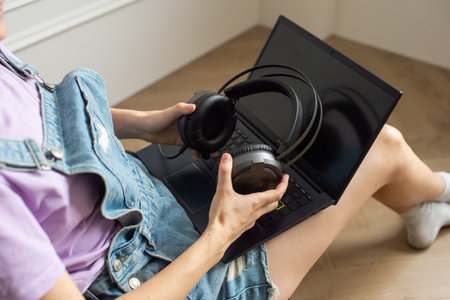 Big black headphones in the hands of a sitting girl near a laptop. Without a faceの写真素材