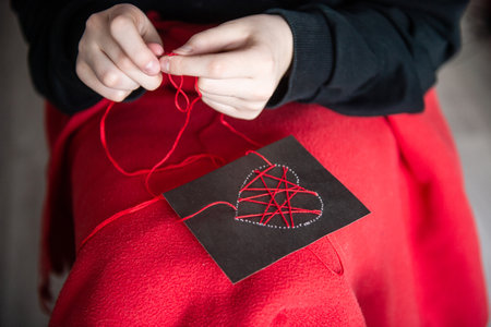 The child's hands make a card with a heart for mother's Day with red threadsの写真素材