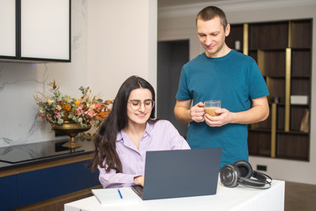 A girl with glasses is sitting and looking at a laptop, a man is standing next to herの写真素材