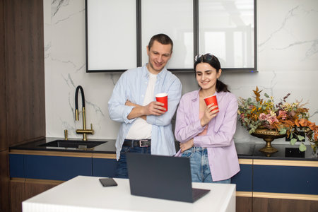 A man and a woman are standing in the kitchen in a coworking with red cups and looking at a laptopの写真素材