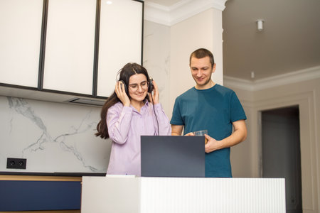 A girl with glasses and headphones looks at a laptop next to a man and laughsの写真素材