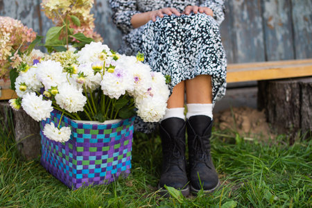 A basket of dahlias and hydrangeas stands near a bench, a man's feetの写真素材