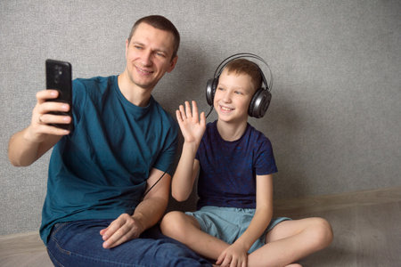 A cute boy with headphones is sitting next to his dad. Make a video callの写真素材