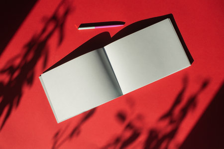 A notepad with a pen lies on a colored red background. Office suppliesの写真素材