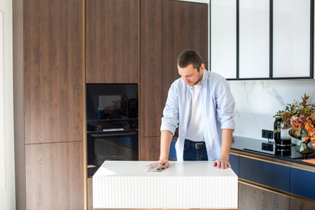 A man wipes a table in the kitchen. Wipe the crumbs off the table with a kitchen towelの写真素材