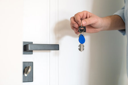 The keys with a chip from the new apartment are in men's hands near the doorの写真素材
