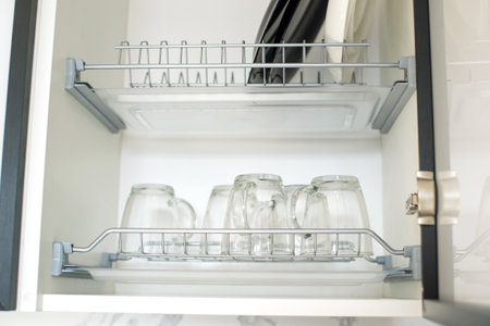 Open kitchen cabinet with dishes, inverted transparent cups and plates