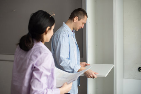 A married couple study the instructions and assemble shelves for the closetの写真素材