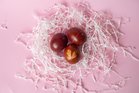 Three painted red eggs with drawings lie in a nest of paper on a pink backgroundの写真素材