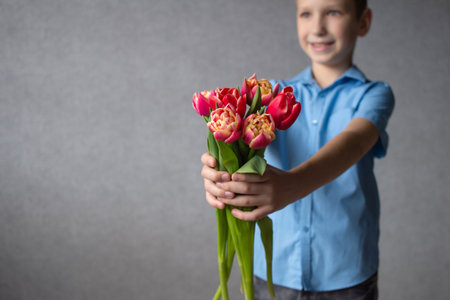 A cute boy stretched out his hands with a colorful bouquet of tulips. mother's day giftの写真素材
