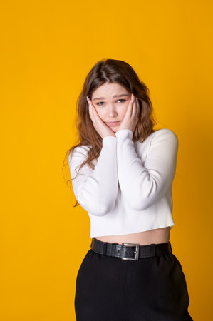 Cute caucasian girl, holding her hands on her face, upset on a yellow backgroundの写真素材