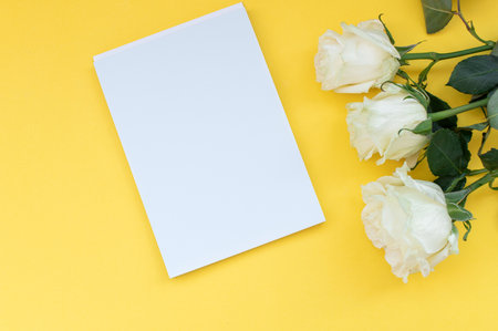 Top view of a yellow table with a mockup of blank notebooks with a bouquet of roses on the side.の写真素材