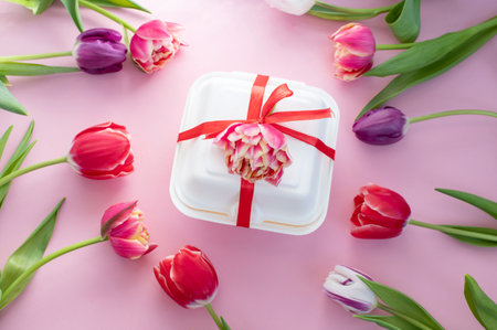 Colorful red double tulips lie around a white gift box with a red ribbon. View from aboveの写真素材