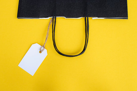 White tag with a paper black bag for recycling on a yellow background. paper bag handles. price...