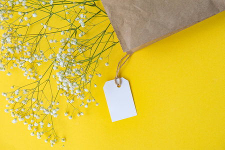 A mock-up of a white tag, label and price tag near a craft bag with flowers lie on a colorful yellow table. Empty space for text. close-upの写真素材