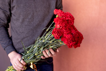 Funeral bouquet of red carnations with a black ribbon in the hands of a manの写真素材