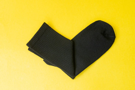 Black cotton socks lie on a yellow table in the shape of a heart.の写真素材
