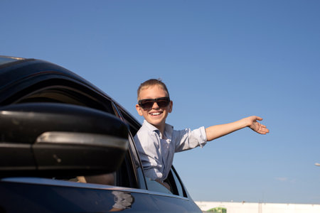 A cute boy in sunglasses looked out of the car window waving and laughing. Climb out of the car...