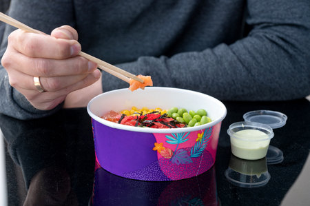 A man eats a delicious colorful healthy natural organic vegetarian Hawaiian poke bowl with Asian...