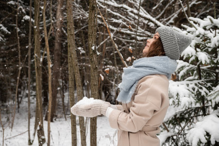 Cute girl in mittens holds snow in winter outside, looks up and smilesの写真素材
