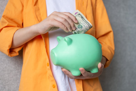 A piggy bank in the hands of a boy in a shirt. Put a banknote in a piggy bankの写真素材