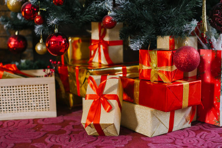 Gold and red gift boxes stand under the Christmas tree near the fireplace on the red carpetの写真素材