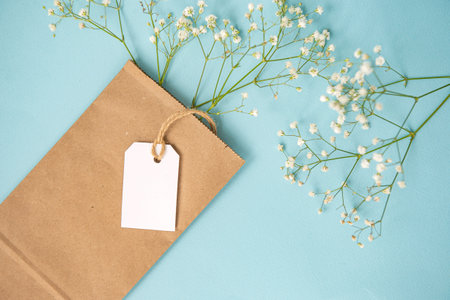 A mock-up of a white tag, label and price tag near a craft bag with flowers lie on a colorful yellow table. Empty space for text. Close-upの写真素材